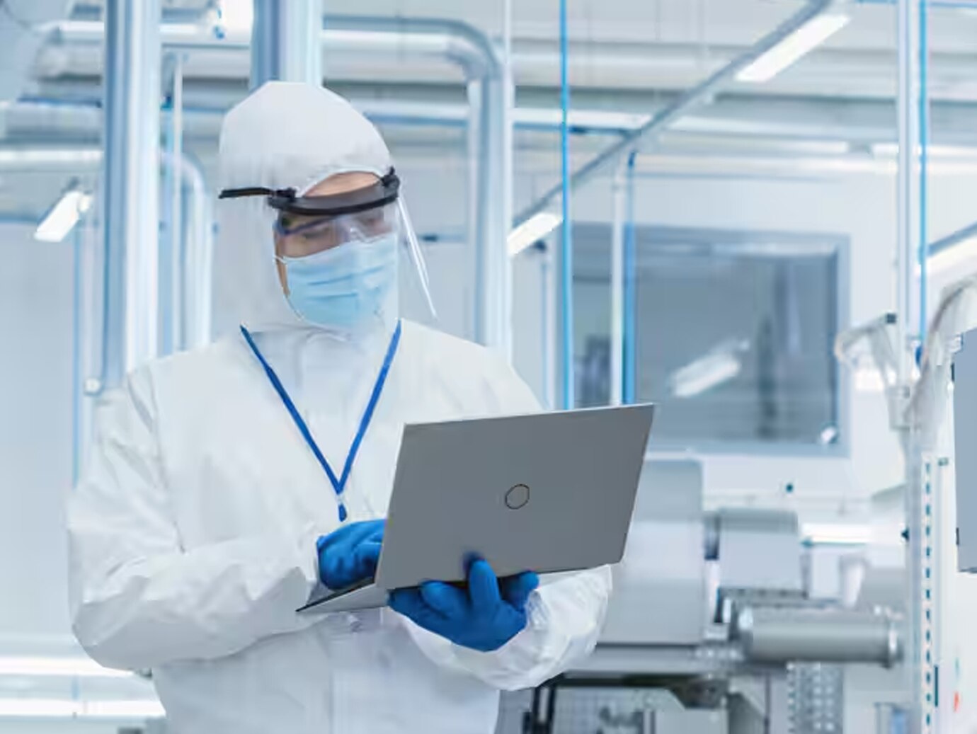 A researcher in protective clothing and mask working on a laptop